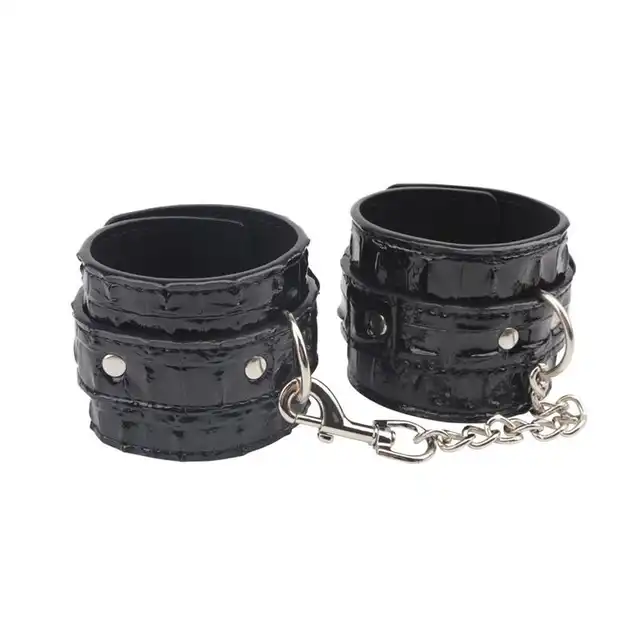 Behave! - Surrender Wrist Restraints. Czarne, wytrzymałe kajdanki z regulacją rozmiaru. Mocno połyskujący materiał