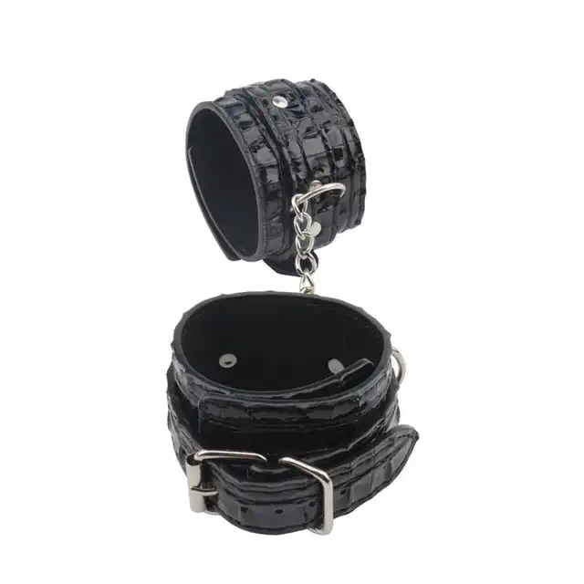 Behave! - Surrender Wrist Restraints. Czarne, wytrzymałe kajdanki z regulacją rozmiaru. Mocno połyskujący materiał